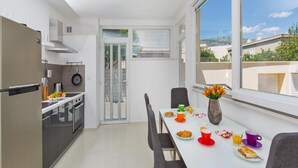 A modern kitchen with a dining area, a large window, and a view of the city. - Apartments St.Thomas - Deluxe Two-Bedroom Apartment (Dubrovnik)