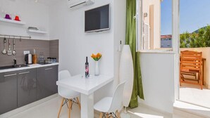 Eine moderne Küche mit Essbereich, einem an der Wand montierten Fernseher und Blick ins Freie durch ein großes Fenster.