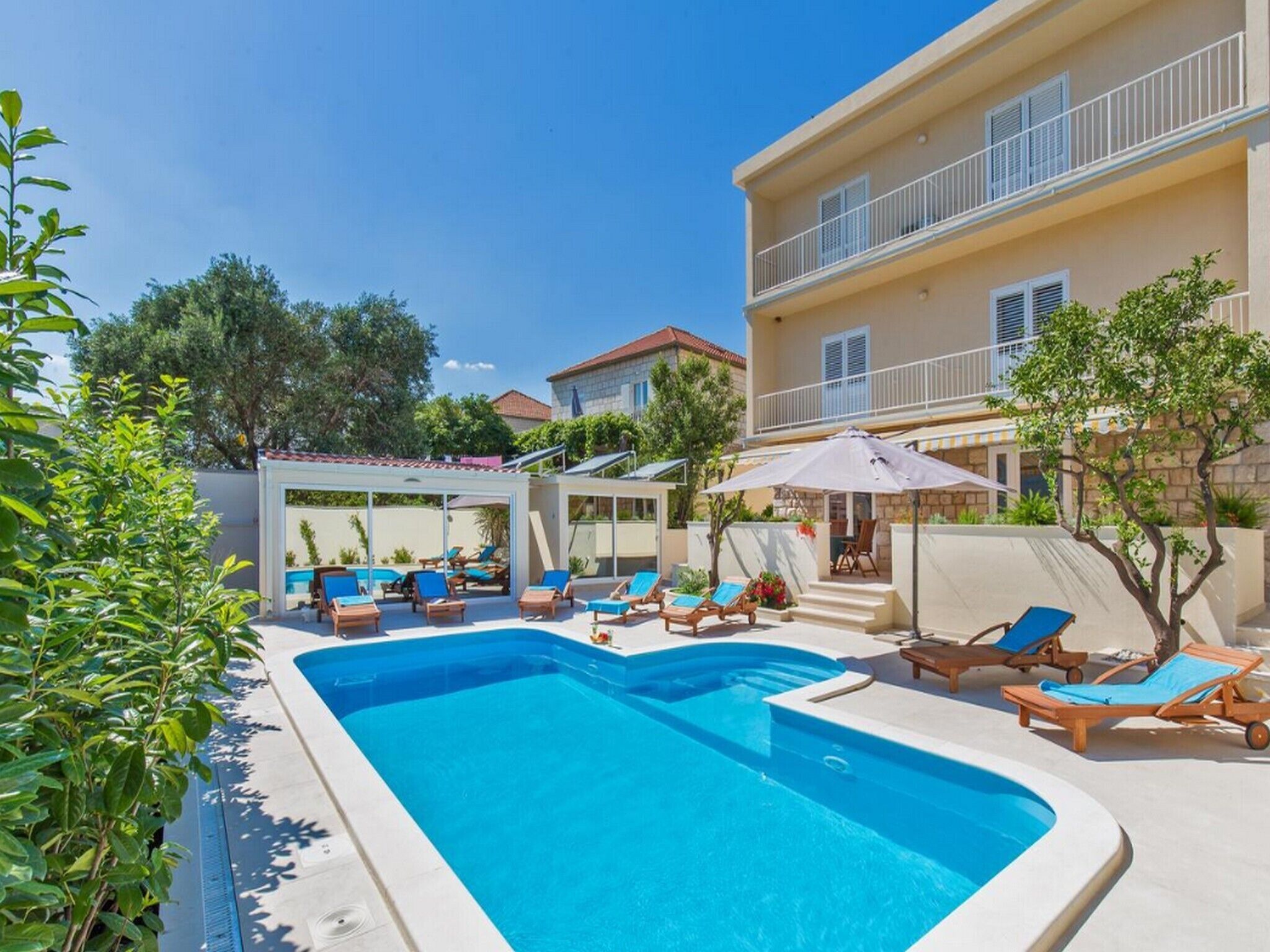 A swimming pool with lounge chairs and umbrellas, surrounded by buildings and greenery.