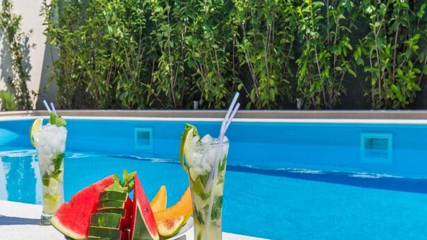 Ein Poolbereich mit einem Tisch, auf dem zwei Getränke und eine Schüssel Wassermelone stehen.