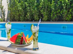 Ambiente à beira da piscina com uma mesa exibindo duas bebidas e uma fatia de melancia.