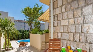 Eine Terrasse im Freien mit einem Holztisch, Stühlen, einem Pool und einer Steinmauer.