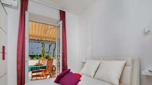 Une chambre à coucher avec un lit, des oreillers, une table avec des chaises et une vue sur un espace extérieur aménagé avec une table et des chaises.