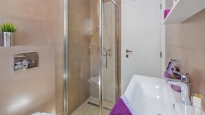 Une salle de bain moderne avec une douche à parois de verre, un lavabo blanc et une serviette violette.