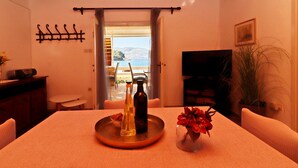 A dining area with a table set for two, a bottle of olive oil, and a vase with red flowers. A TV is mounted on the wall, and a plant is visible in the corner. - Holiday Home Neda - Three-Bedroom Holiday Home with Terrace and Sea View (Vela Luka)