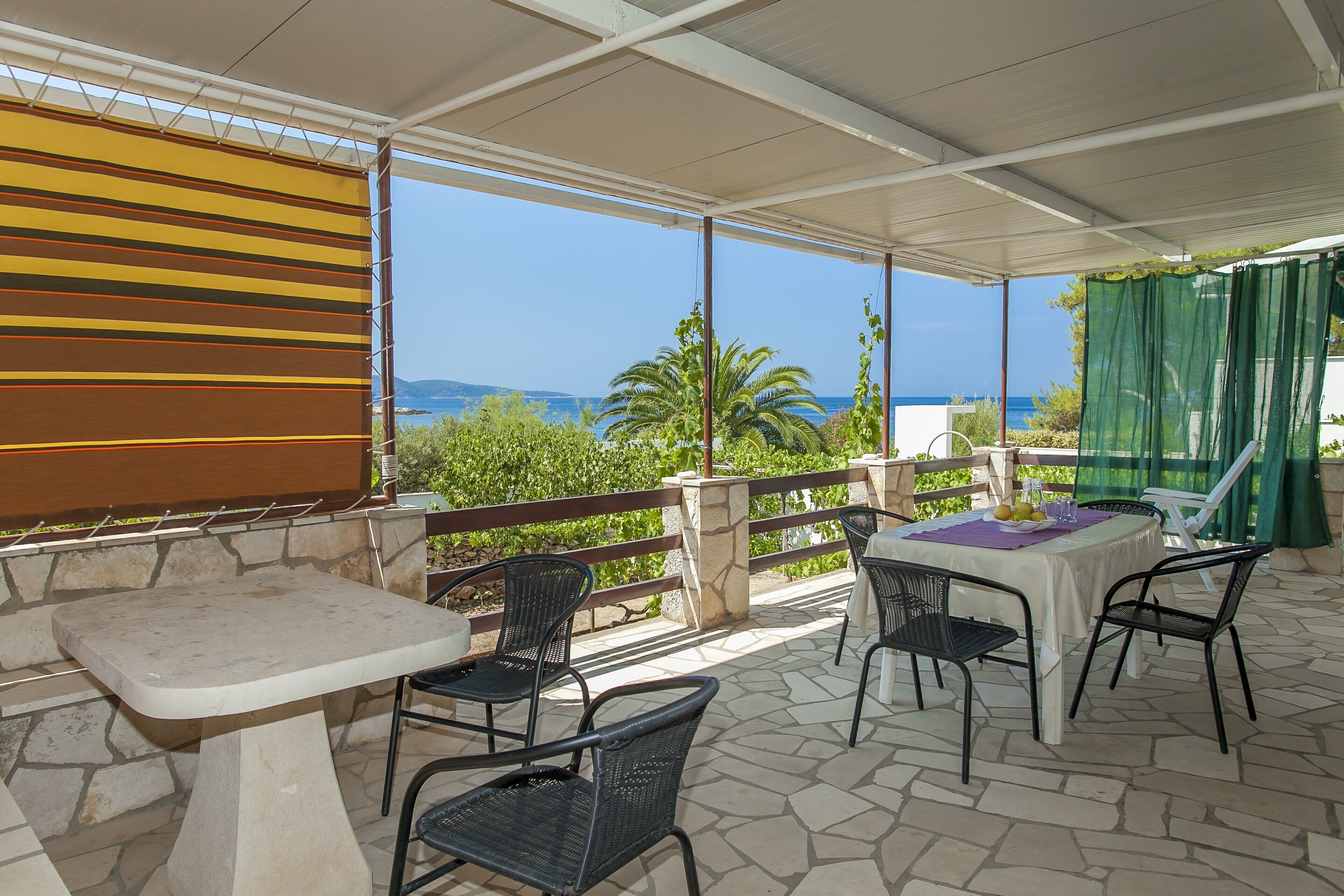 An outdoor patio with a table and chairs, a view of the sea, and a striped awning.