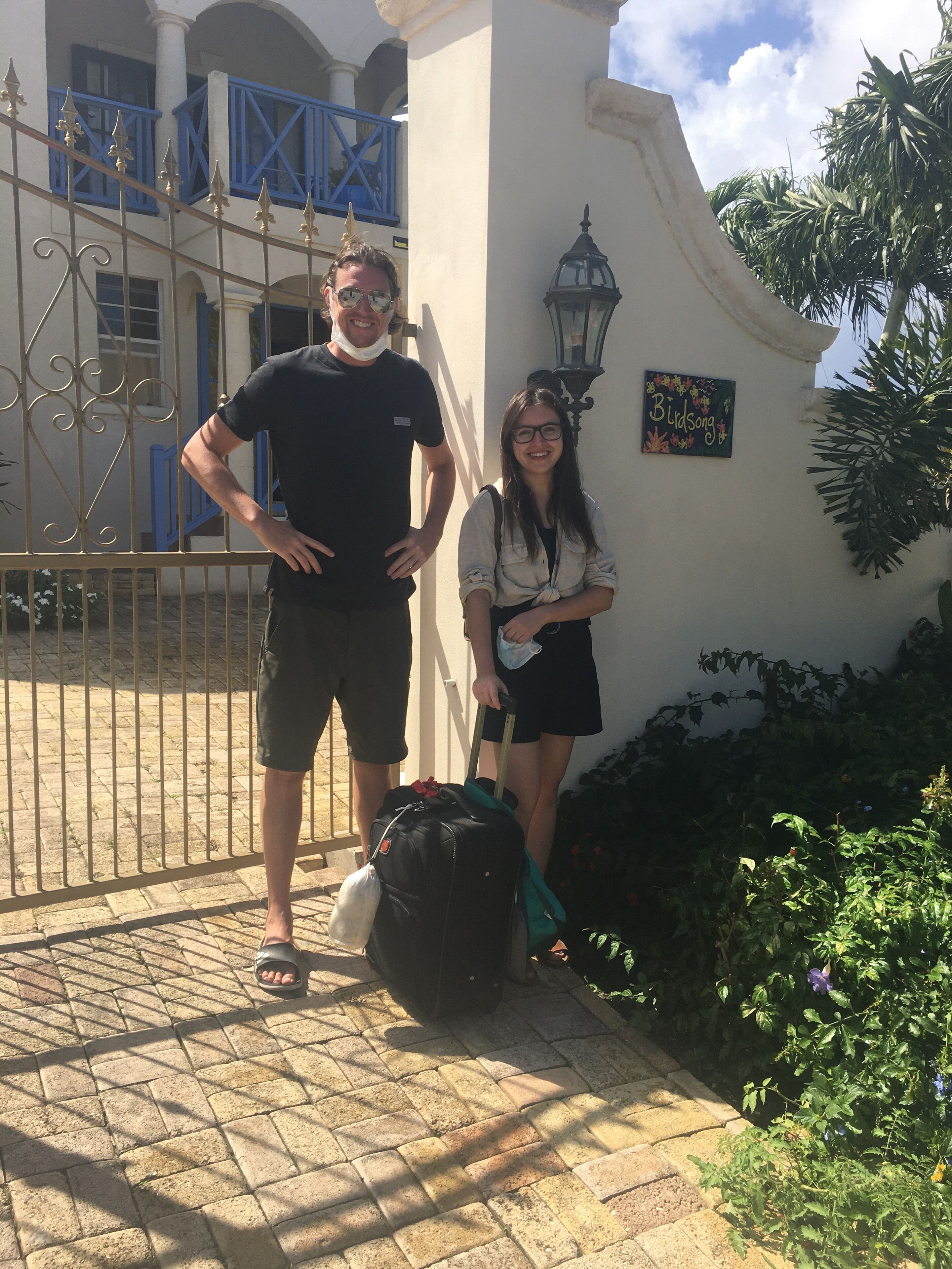Two people standing in front of a building with a gate, a wall with a sign, and a lamp post.