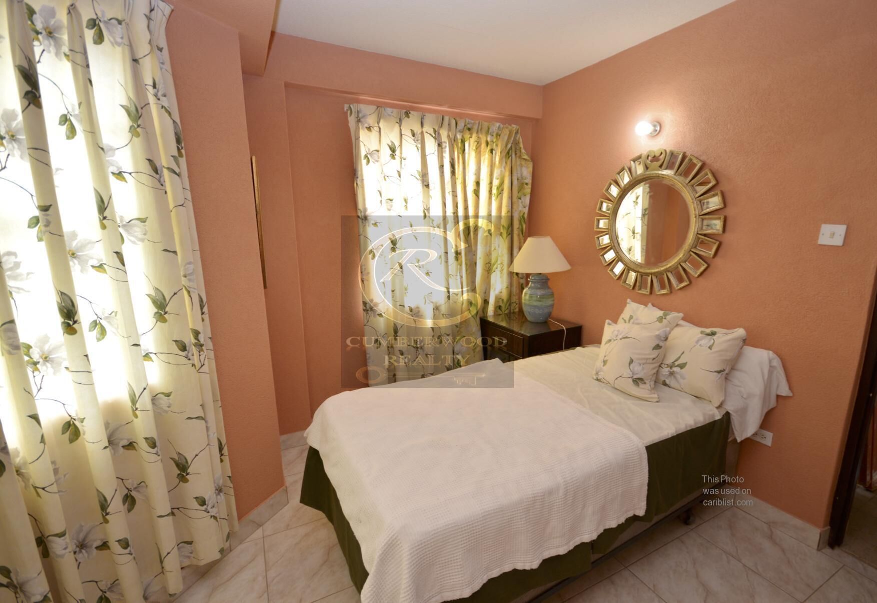 A bedroom with a bed, a nightstand, a lamp, a mirror, and floral curtains.