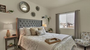 Une chambre à coucher avec un grand lit, une table de chevet avec une lampe, une chaise et une fenêtre avec des rideaux.