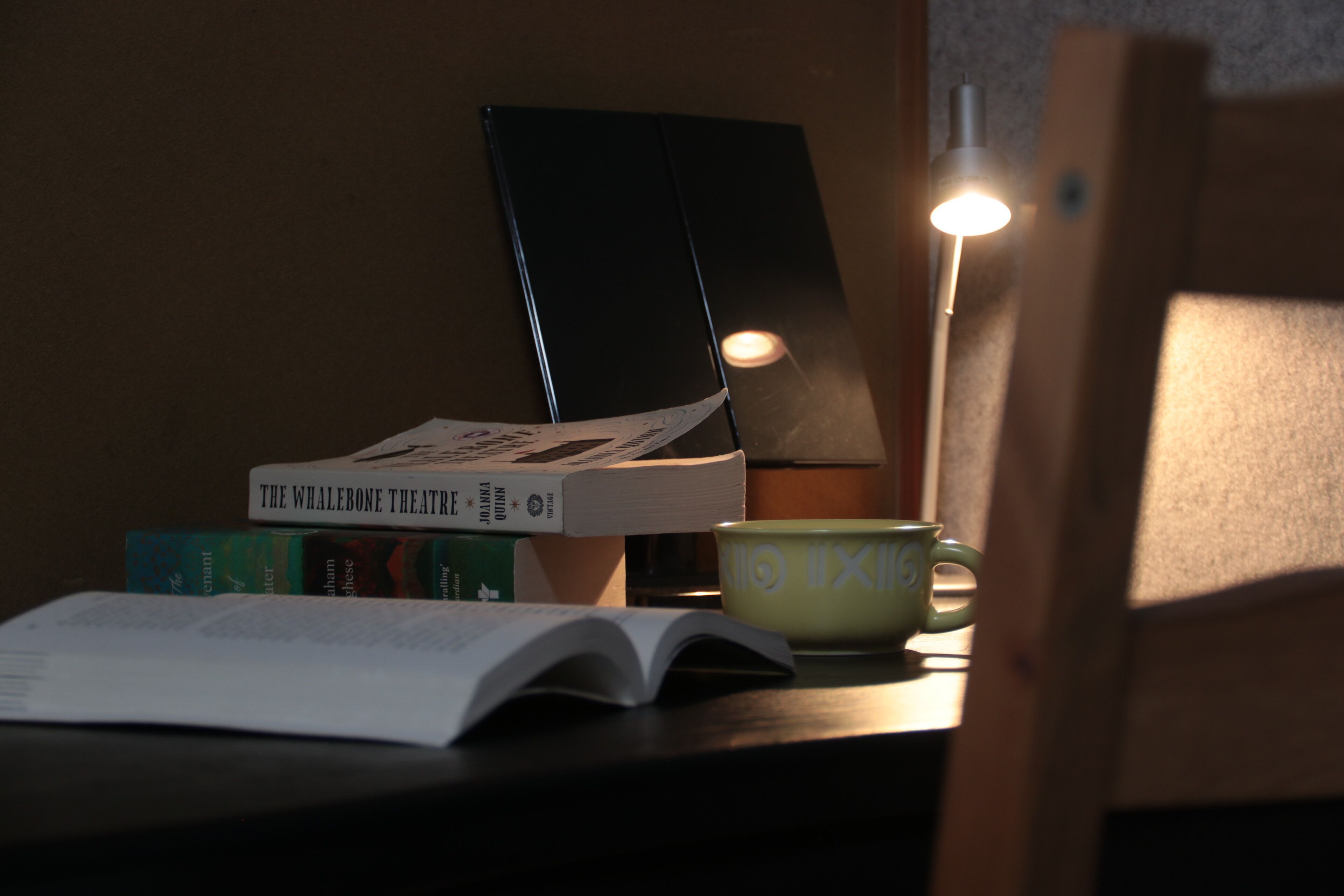 A desk with books, a cup, and a lamp.