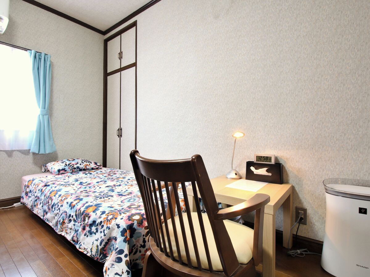 A bedroom with a bed, a desk with a chair, a lamp, a clock, and a washing machine.