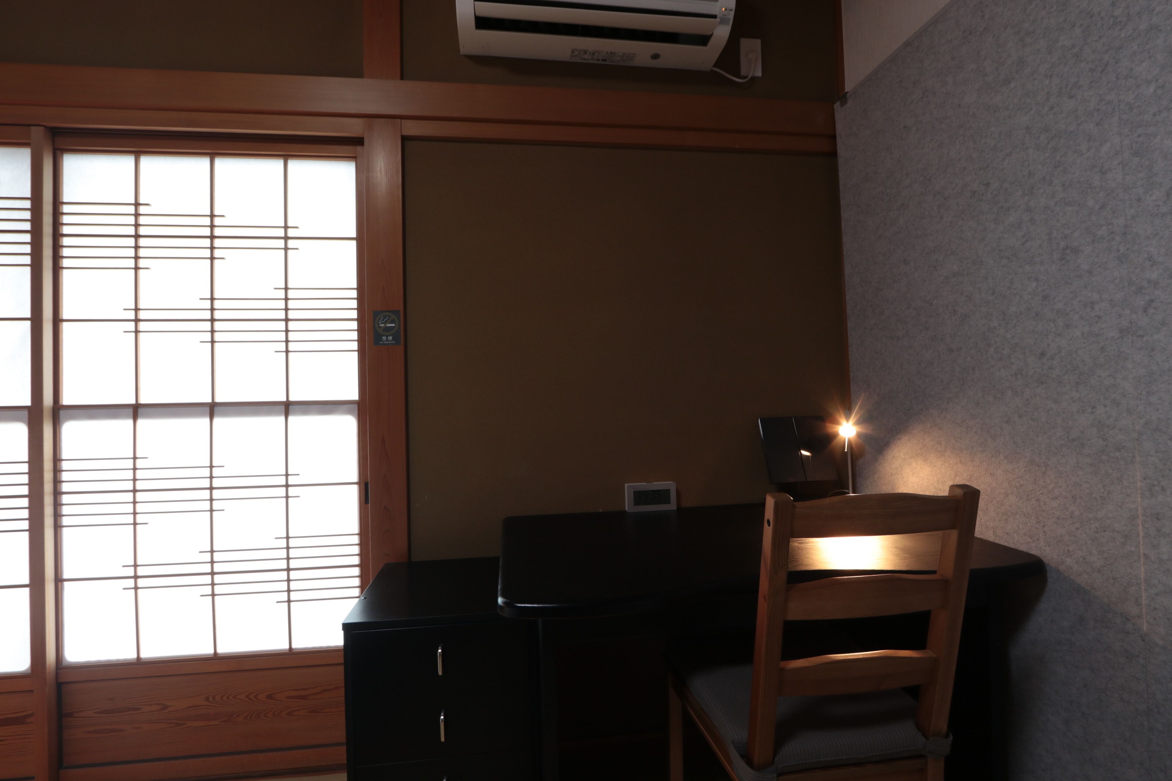 A room with a sliding shoji screen door, a desk with a chair, and a wall-mounted air conditioner.