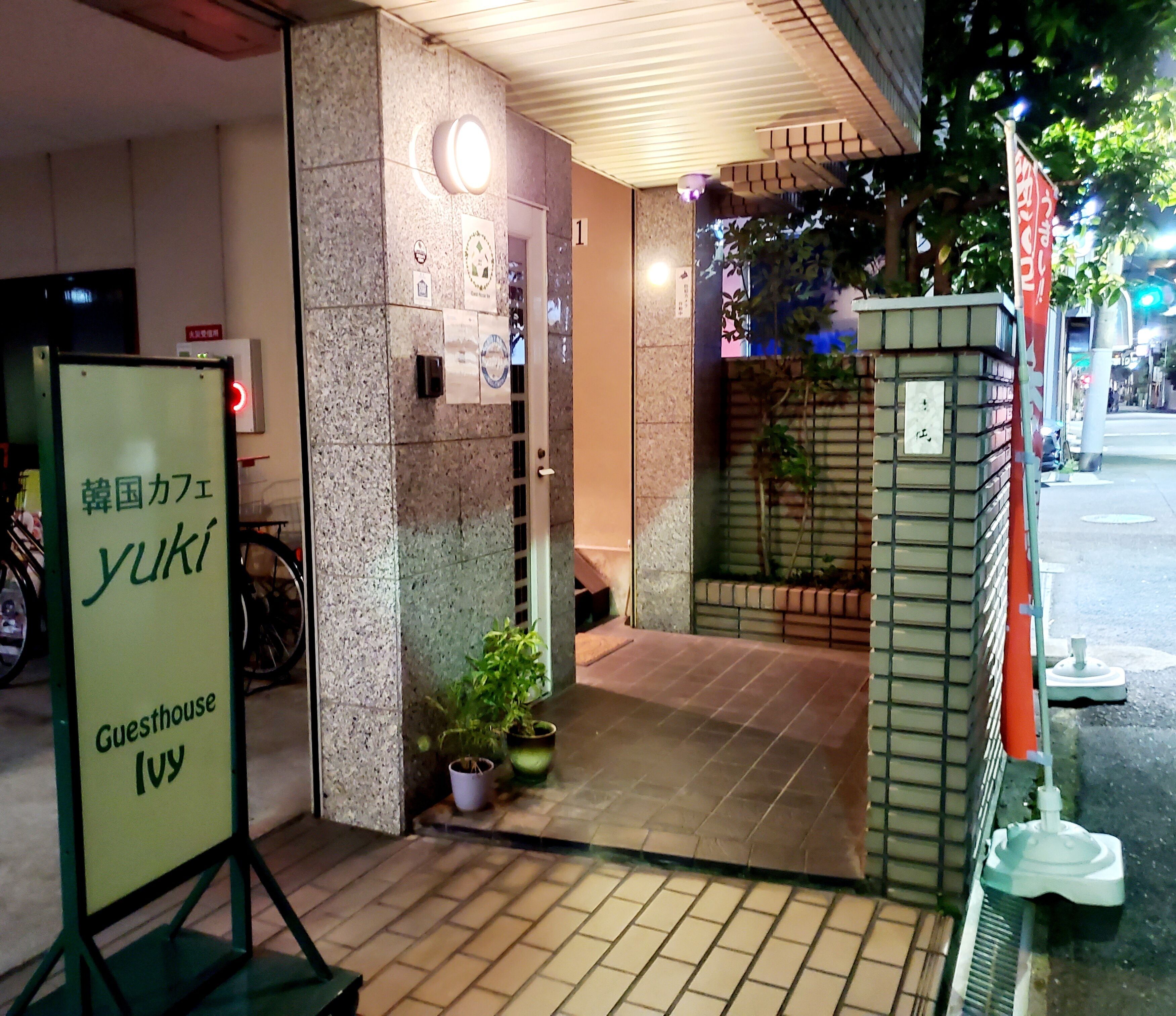 A guesthouse entrance with a signboard, a potted plant, and a tiled entrance.