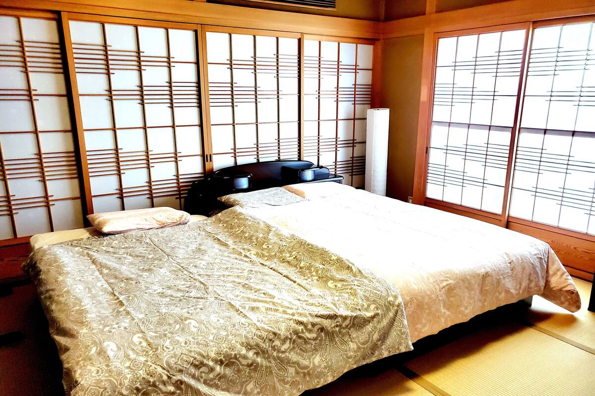 A traditional Japanese-style room with tatami flooring, a bed with a patterned bedspread, and shoji screens.