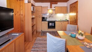 A compact kitchen with wooden cabinets, a microwave, and a stove. There's a dining area with a table and chairs, and a television on the left. - Apartment Laura by Interhome (Zell am Ziller)