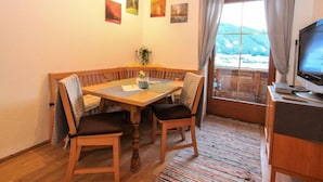 A cozy dining area with a wooden table and chairs, a television on a stand, and a window with curtains. - Apartment Laura by Interhome (Zell am Ziller)