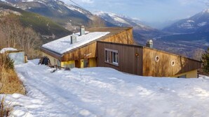 A wooden cabin with a sloped roof, surrounded by snow-covered ground and mountains in the background. - Maison Le Fontany by Interhome (Crans-Montana)
