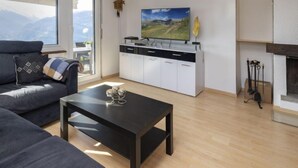 A modern living room with a sofa, a coffee table, and a TV on a white cabinet. - Maison Le Fontany by Interhome (Crans-Montana)