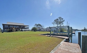 A grassy area with a dock extending into a body of water, a building with a flat roof, and a clear sky.