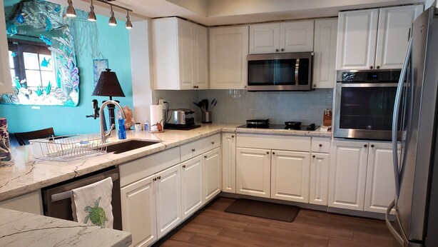 A modern kitchen with white cabinets, stainless steel appliances, and a wooden floor.