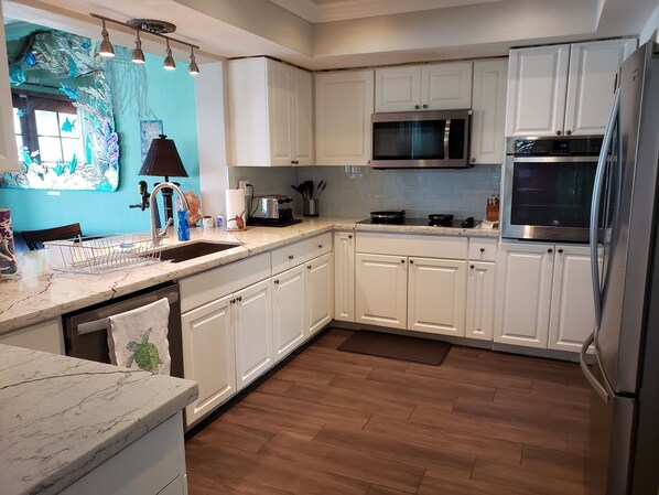 A modern kitchen with white cabinets, stainless steel appliances, and a wooden floor.