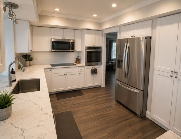 A modern kitchen with white cabinets, stainless steel appliances, a marble countertop, and a wooden floor.