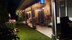 A covered outdoor seating area with string lights, a lawn, and a patio table.