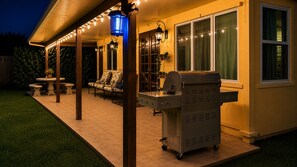 A covered patio with a grill, outdoor furniture, and string lights.