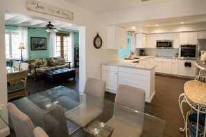 A modern kitchen with white cabinets, a microwave, oven, and a dining area with a glass table and chairs.