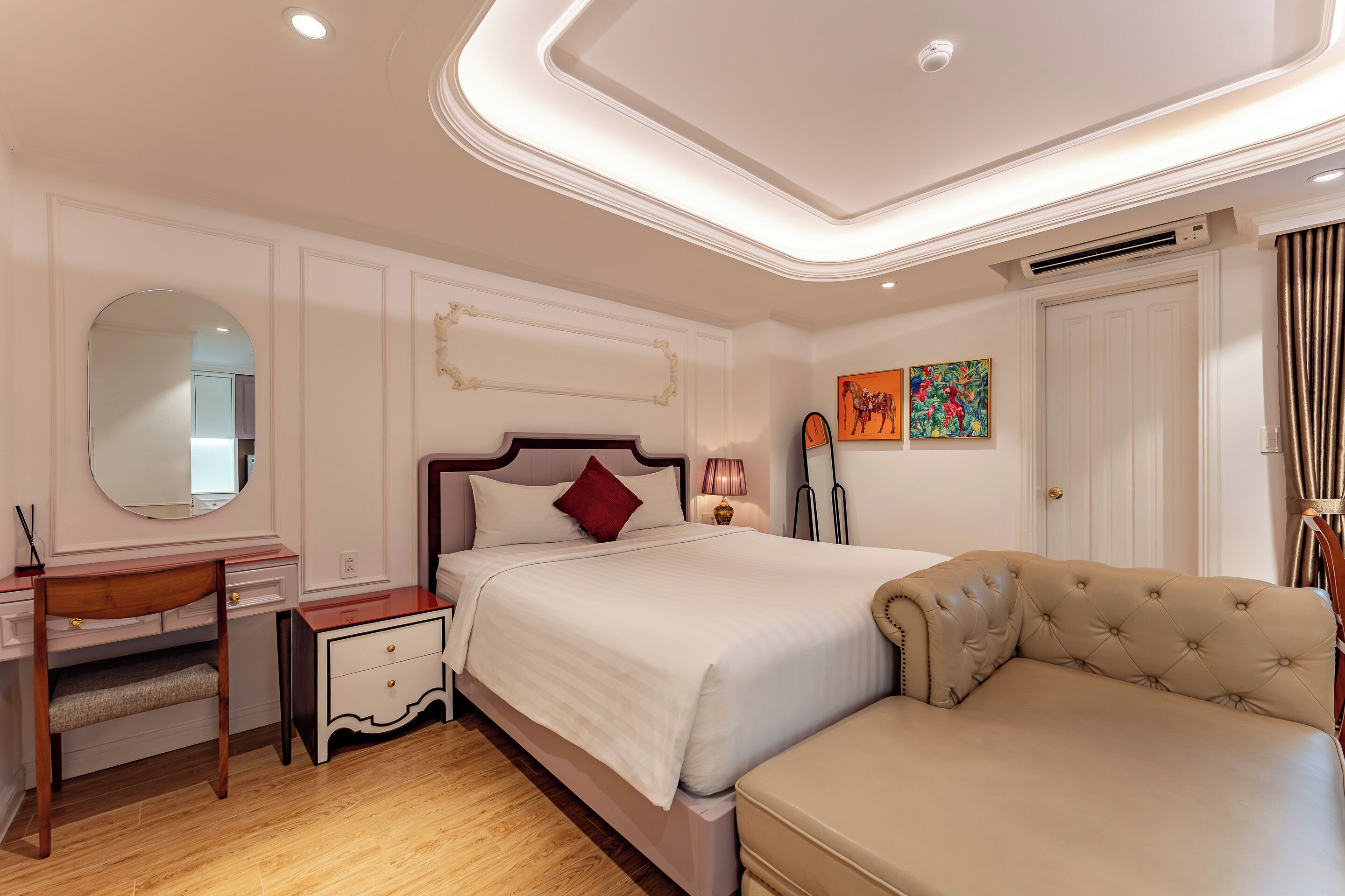 A bedroom with a bed, bedside table, vanity, and a sofa.