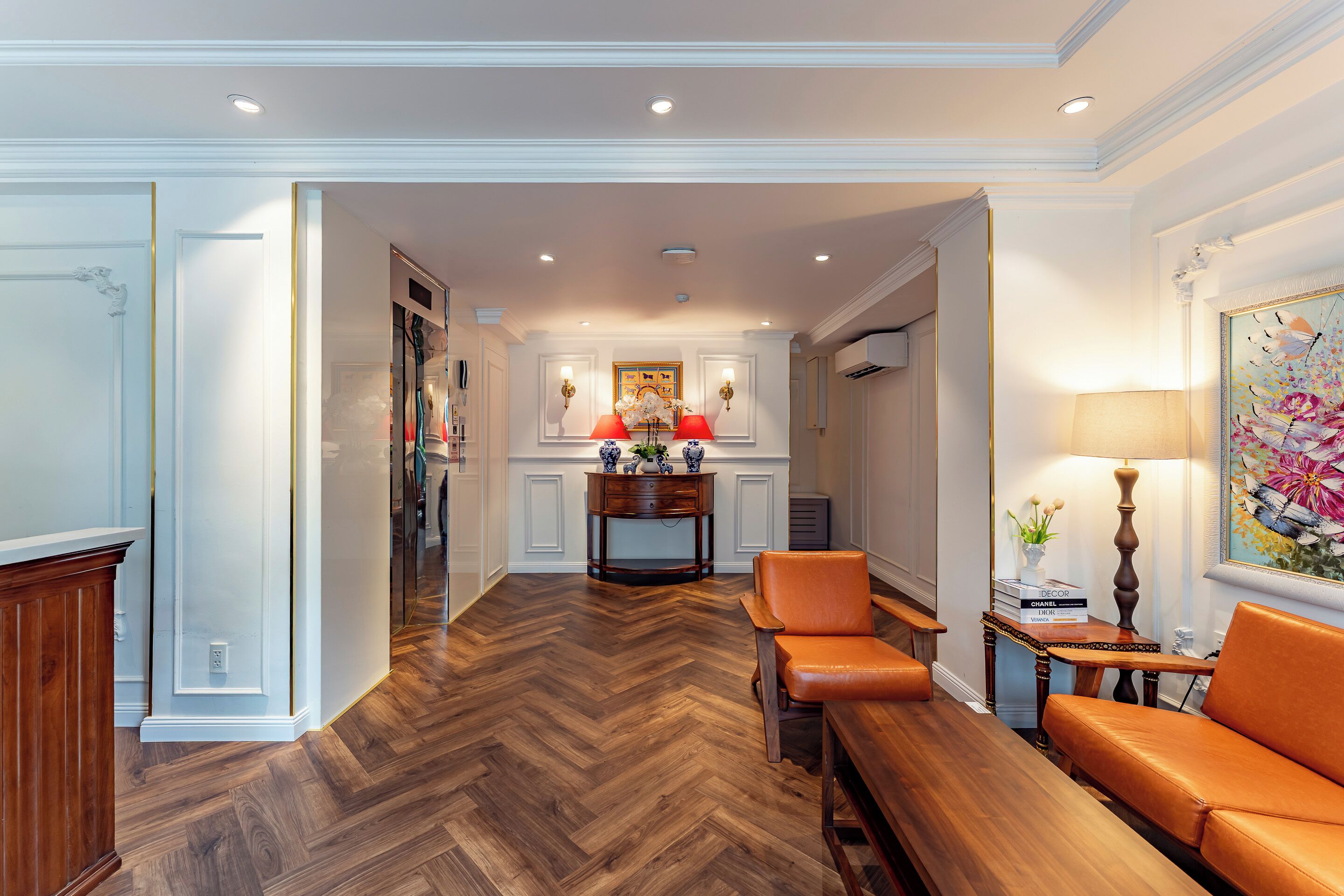 A spacious living area with a herringbone wood floor, a leather sofa, a wooden coffee table, and a side table with a lamp.