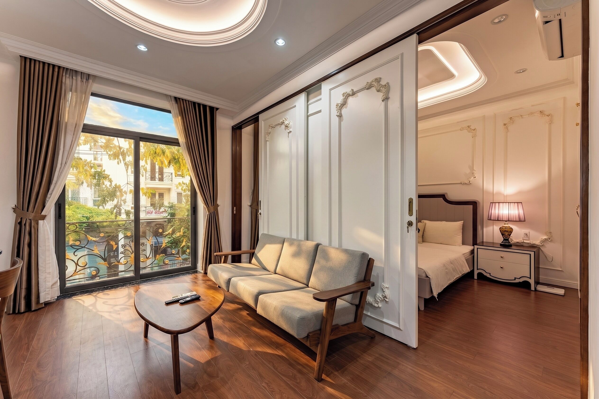 A hotel room with a sofa, a small table, a bed, a nightstand, and a view of the outside.