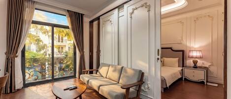 A hotel room with a sofa, a small table, a bed, a nightstand, and a view of the outside.