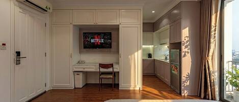 Habitación de hotel con cama, escritorio, silla, televisor y kitchenette.