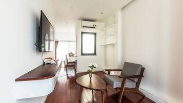 Una sala de estar moderna con piso de madera, una mesa de centro redonda, un sillón gris, un televisor de pantalla plana montado en la pared y un pequeño florero con flores sobre la mesa.