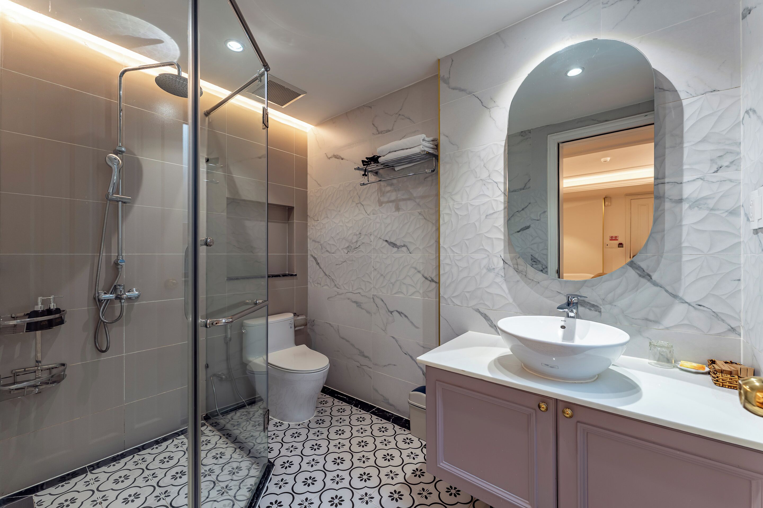 Un baño moderno con ducha envuelta en vidrio, lavamanos blanco y pared con estampado de mármol.
