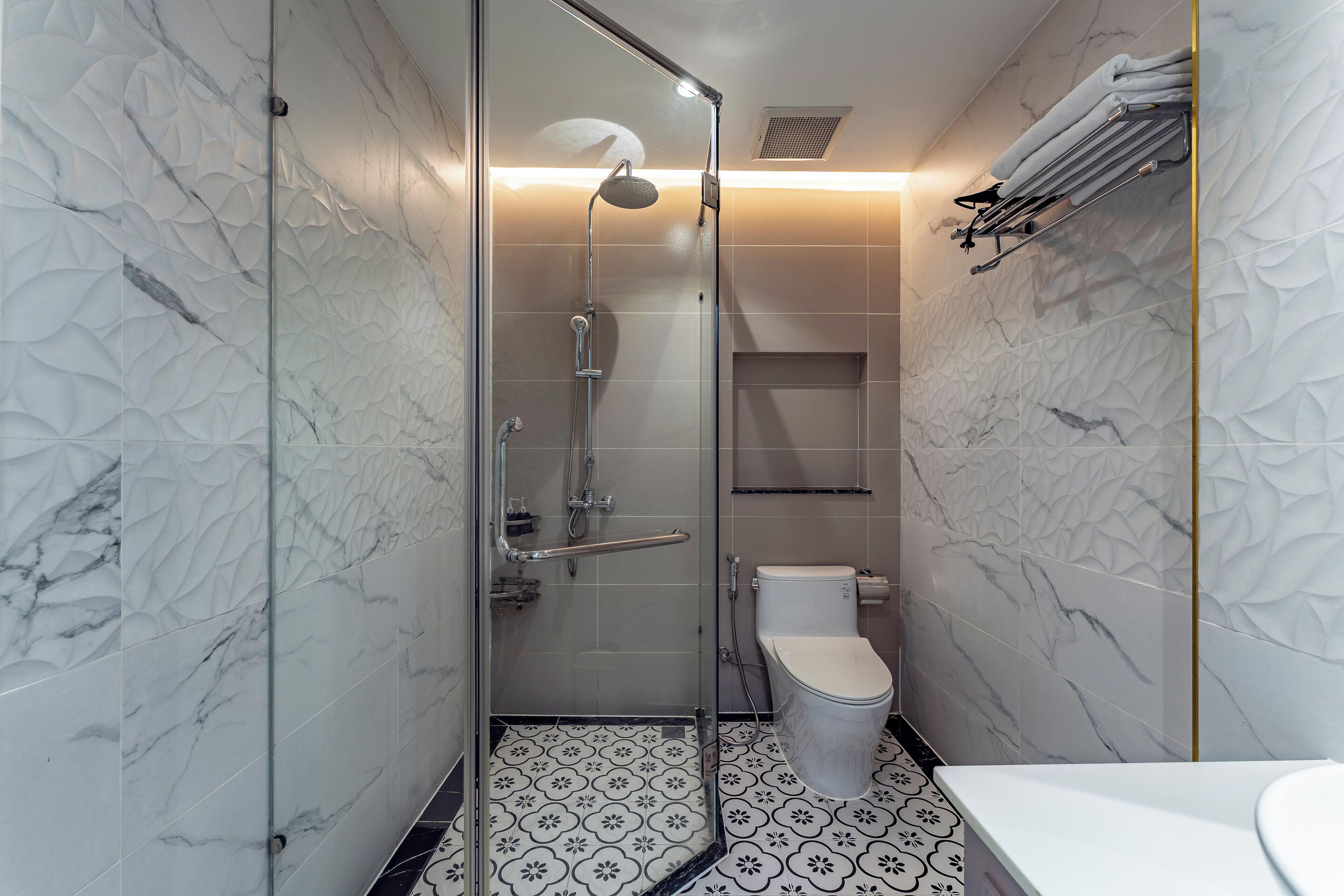 Un baño moderno con cabina de ducha de vidrio, inodoro blanco y lavamanos sobre encimera blanca.