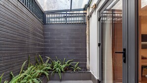 Un espacio exterior moderno con un revestimiento de madera oscura, un ventanal de vidrio y suelo de baldosas.