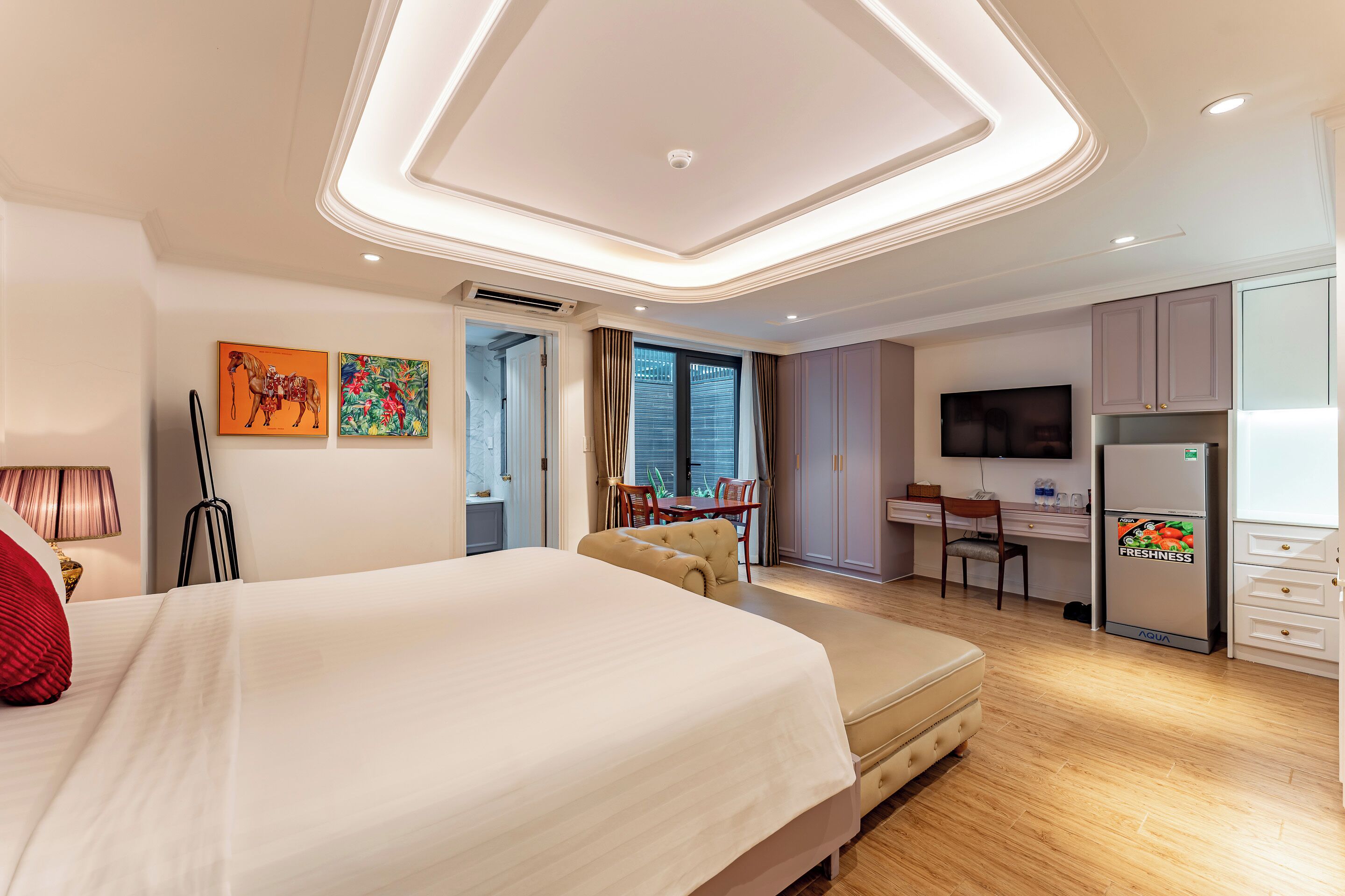 A hotel room with a large bed, a desk, a television, and a minibar.