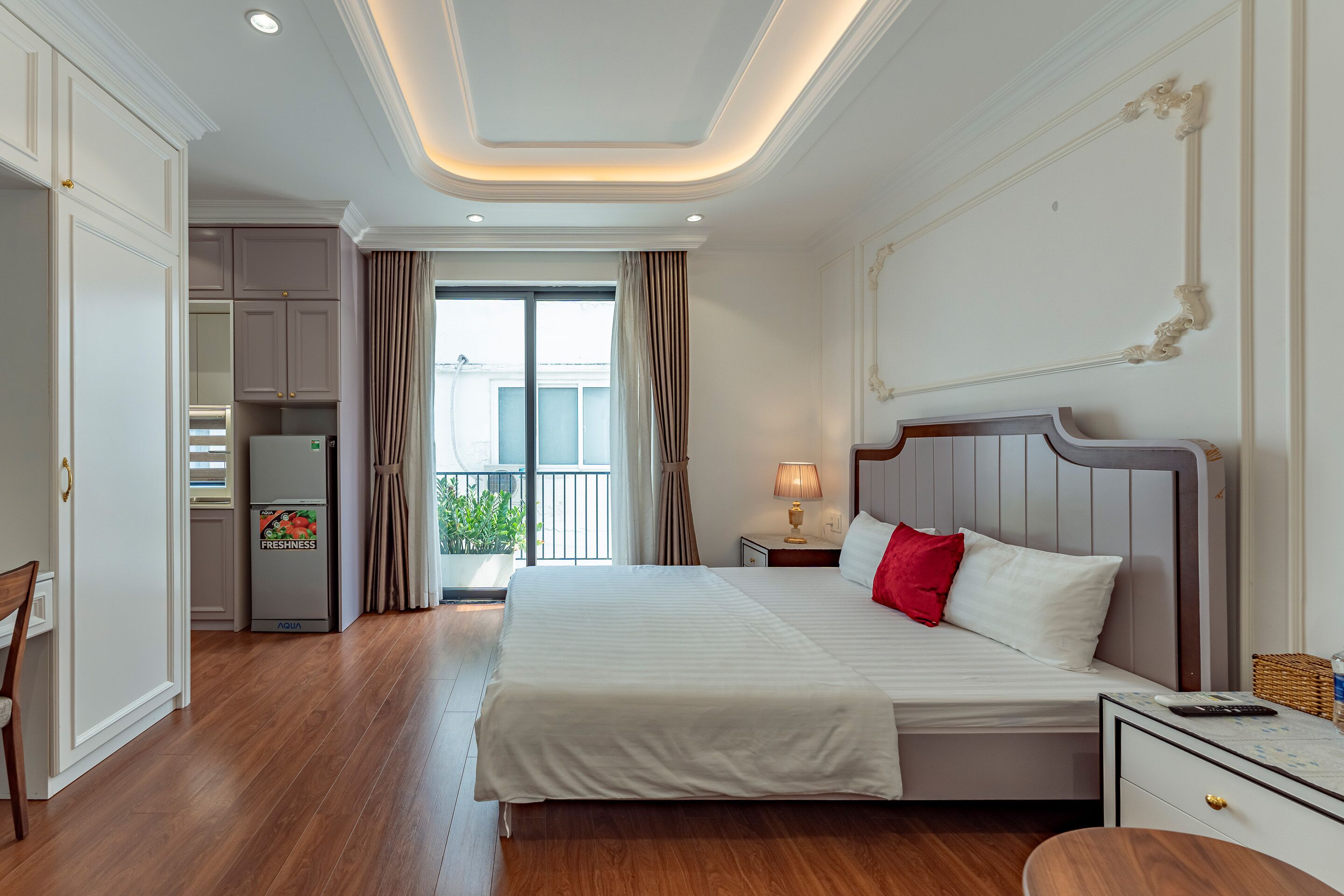 A hotel room with a large bed, a bedside table, a nightstand, a chair, a wardrobe, and a balcony with curtains.