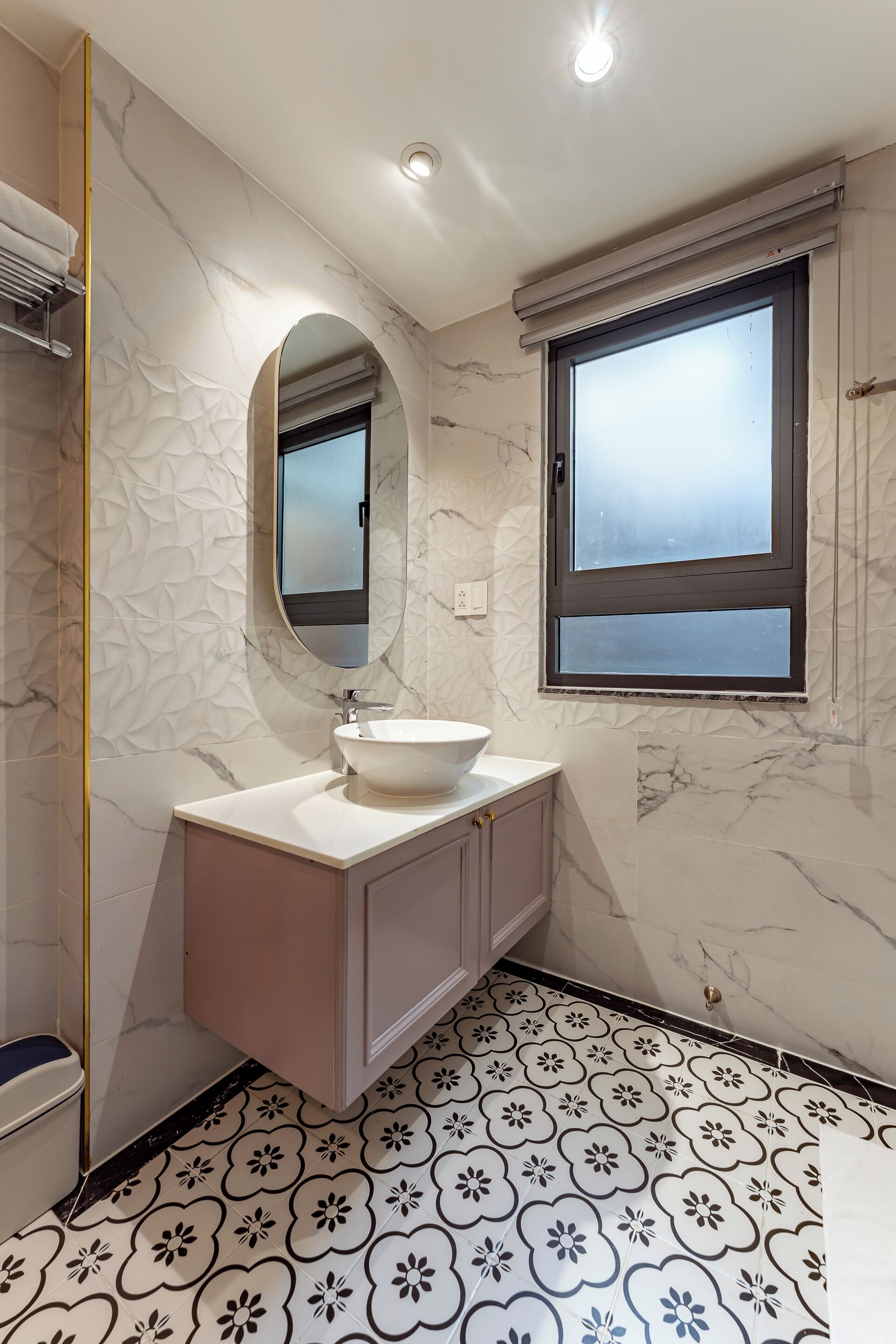 A bathroom with a marble wall, a sink, a mirror, and a window.