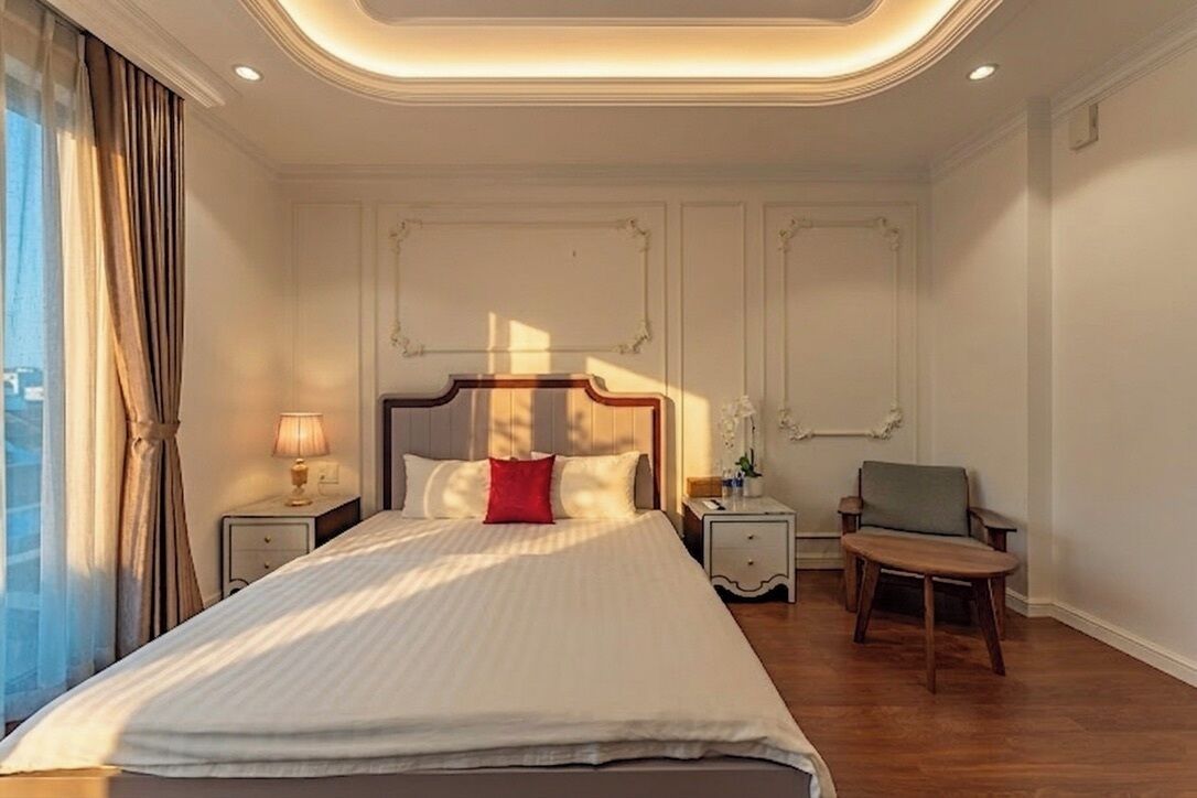 Habitación de hotel con una cama grande, dos mesitas de noche, una silla y una ventana con cortinas.
