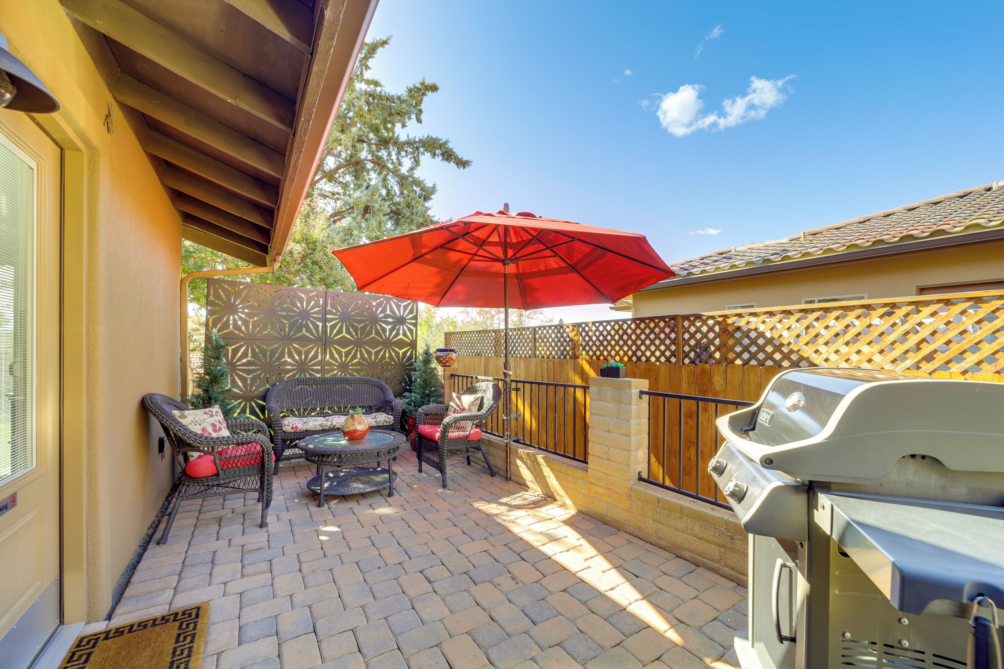 Une terrasse avec des meubles d’extérieur, un barbecue et un parasol rouge.