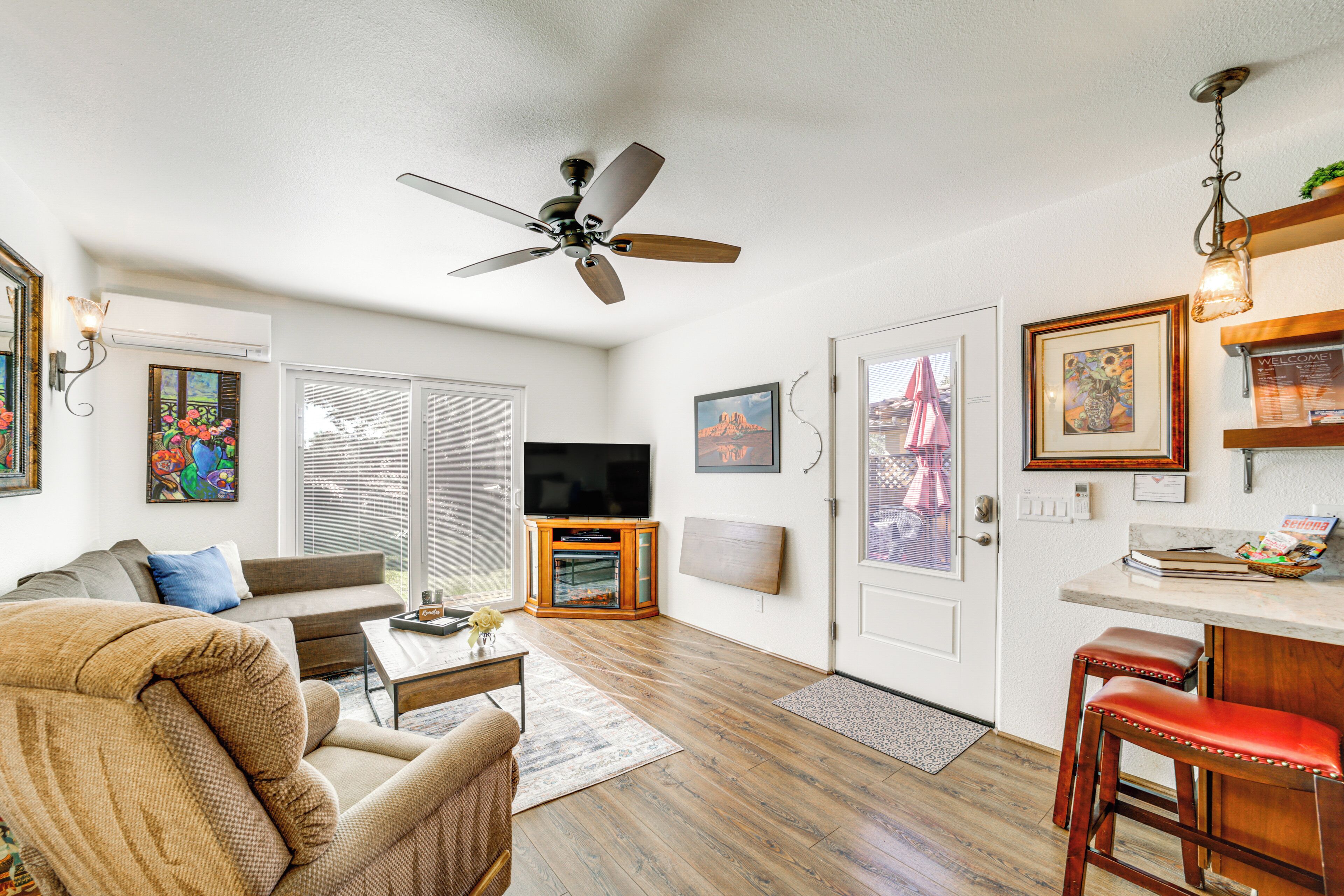 A spacious living room with a ceiling fan, a flat-screen TV, a sofa, a coffee table, and a dining area with bar stools.