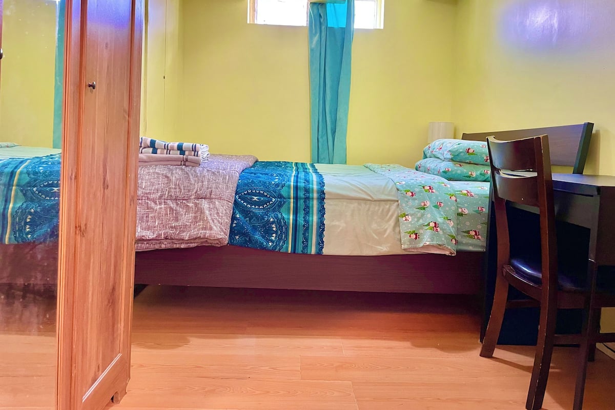 Una habitación con cama, escritorio y silla. Hay dos ventanas con cortinas.