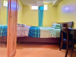 A room with a bed, a desk, and a chair. There are two windows with curtains.