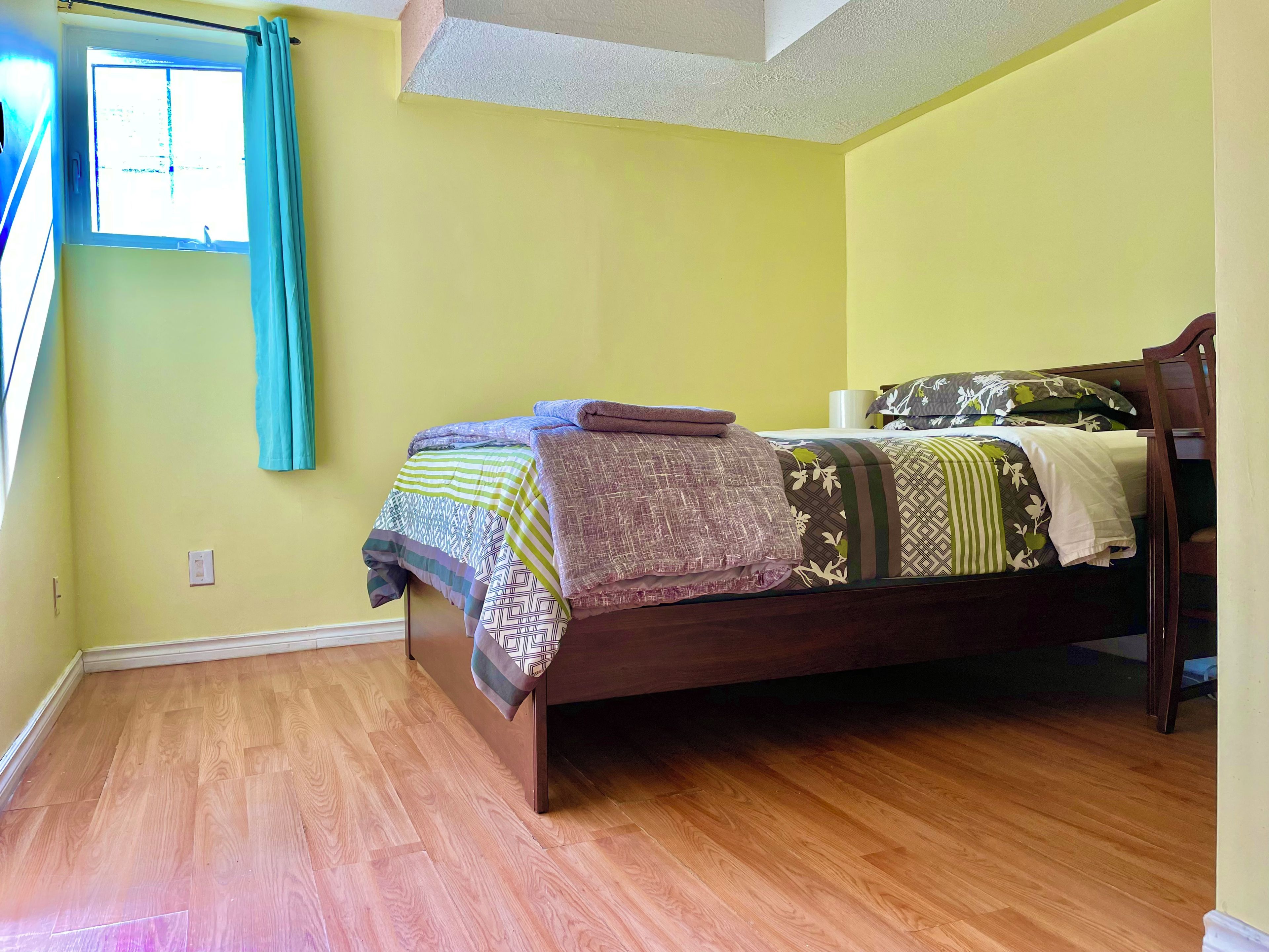 A bedroom with a wooden bed, a window with curtains, and a wooden floor.