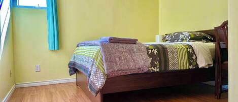 A bedroom with a wooden bed, a window with curtains, and a wooden floor.
