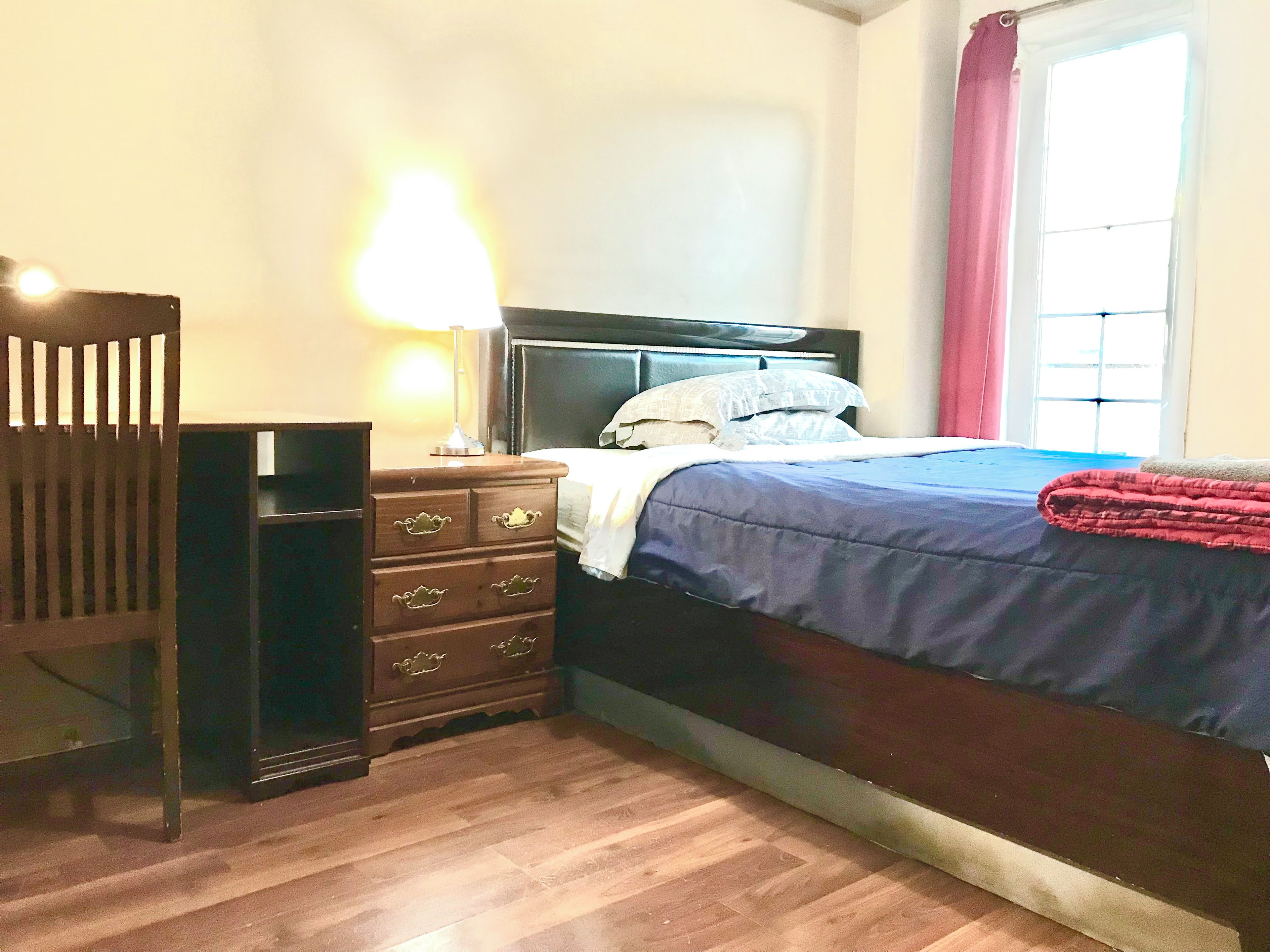 A bedroom with a bed, a dresser, a lamp, and a window with curtains.