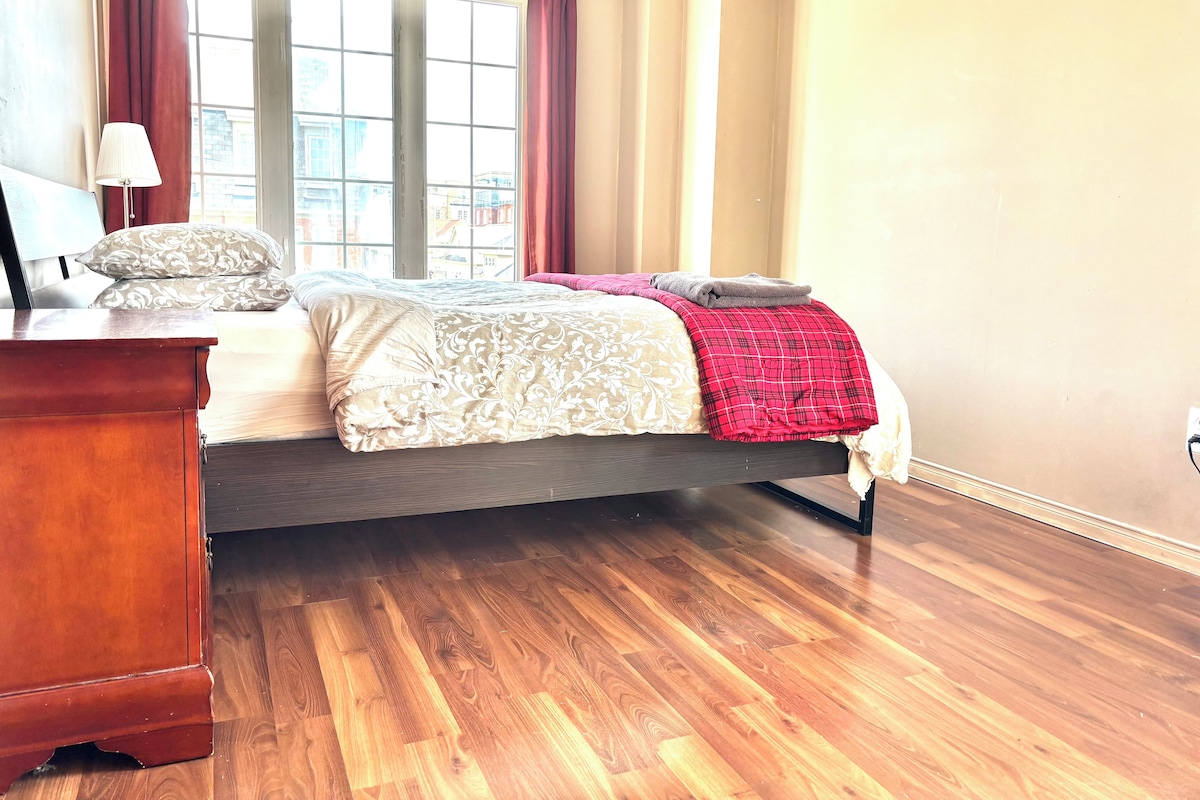 Un dormitorio con cama, cómoda de madera, ventana con cortinas y lámpara.